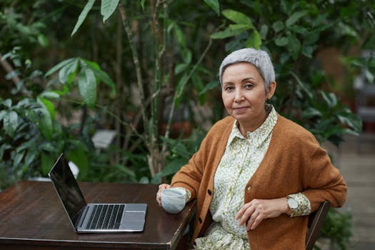 Elderly woman with laptop enjoying coffee in outdoor garden workspace.