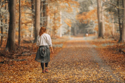 A woman strolls on a leaf-covered path through an enchanting autumn forest.