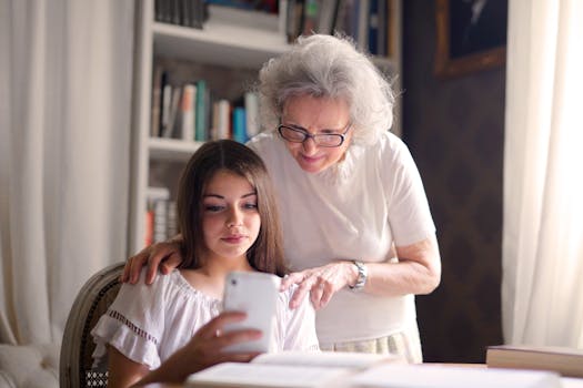 Senior woman guiding teenager on smartphone indoors, fostering learning and connection.