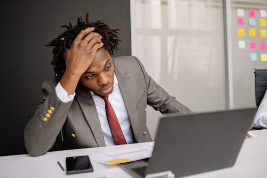 Businessman with dreadlocks looking worried while working on a laptop in the office.